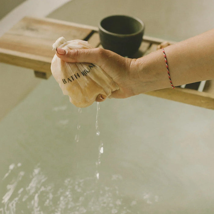 woman in bath tub with a cup of tea and a bag of bath herbs