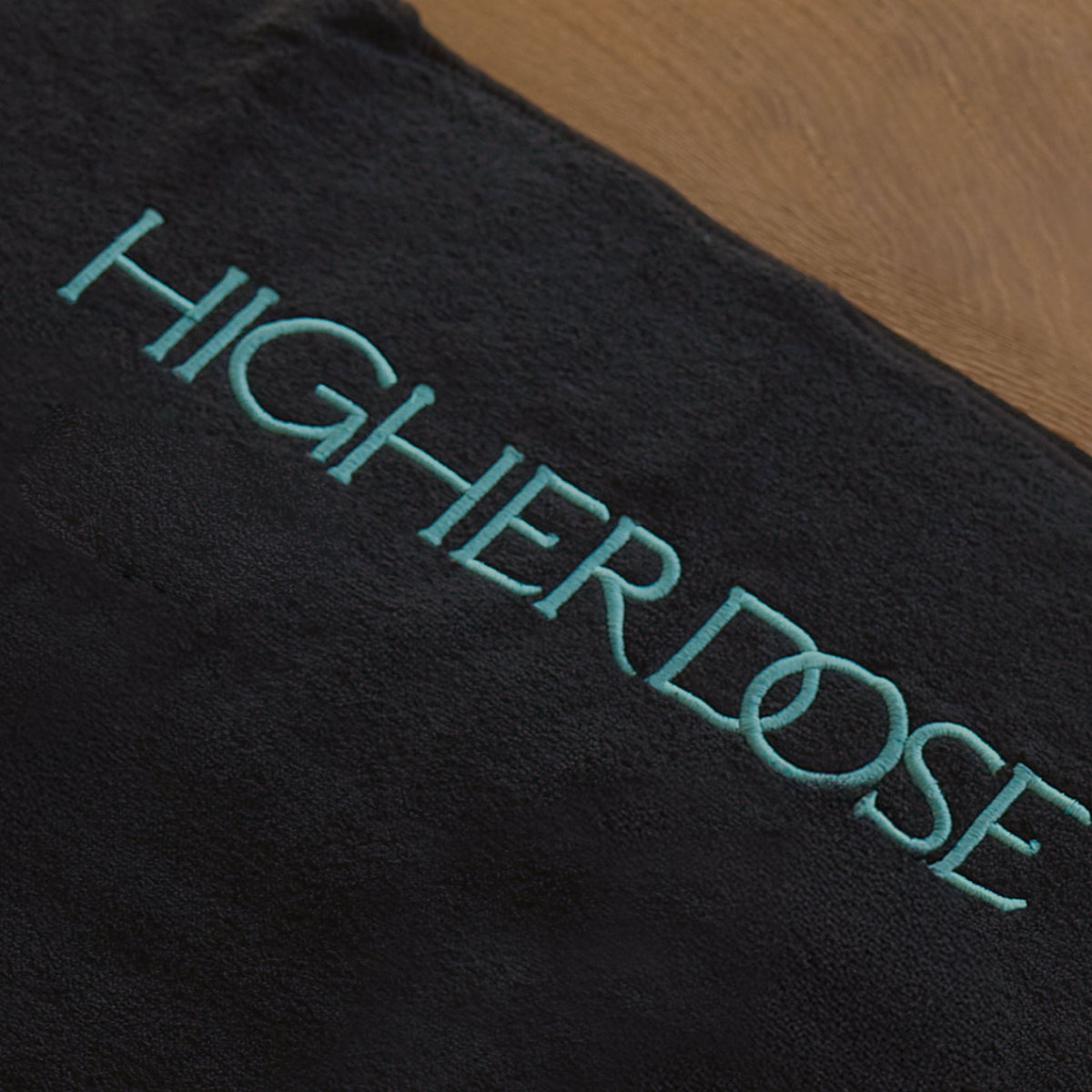 Close-up of the HigherDOSE towel topper logo embroidered in teal on a black towel