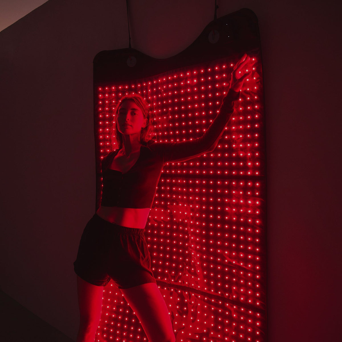 Woman lying against the hung HigherDOSE Full Body Red Light Mat glowing red