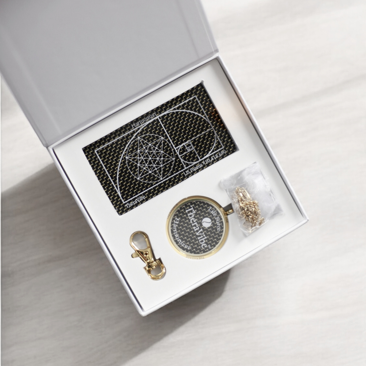Open Therasage TheraVibe box set holding the Quantum Card, gold pendant, clasp and chain, angled view