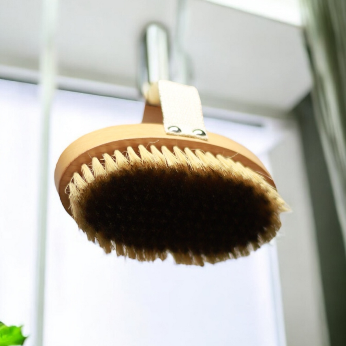 Therasage TheraBrush dry brush with cotton hand strap and bristles facing up near a window