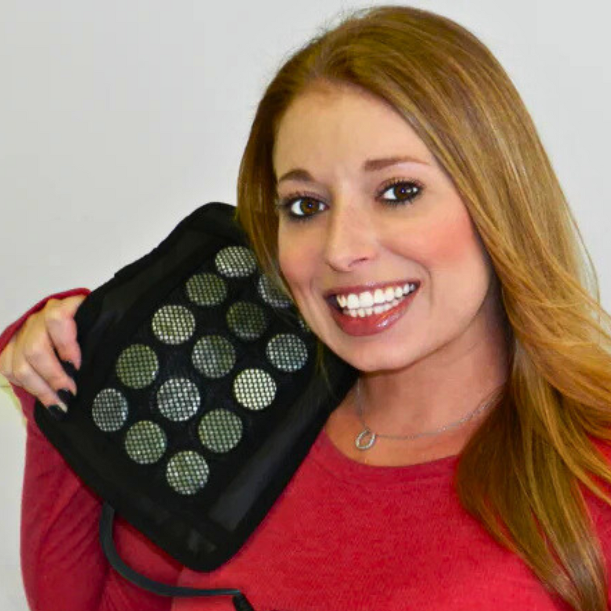 Smiling woman holding a Therasage Healing Pad Mini Square against her cheek