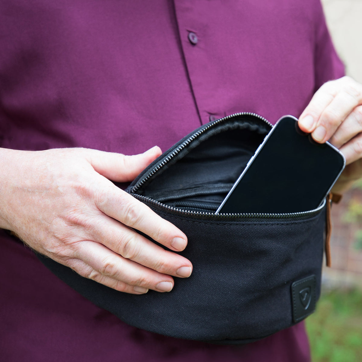 Hands pulling a phone out of the open Shield Your Body Canvas Traveler Fanny Pack