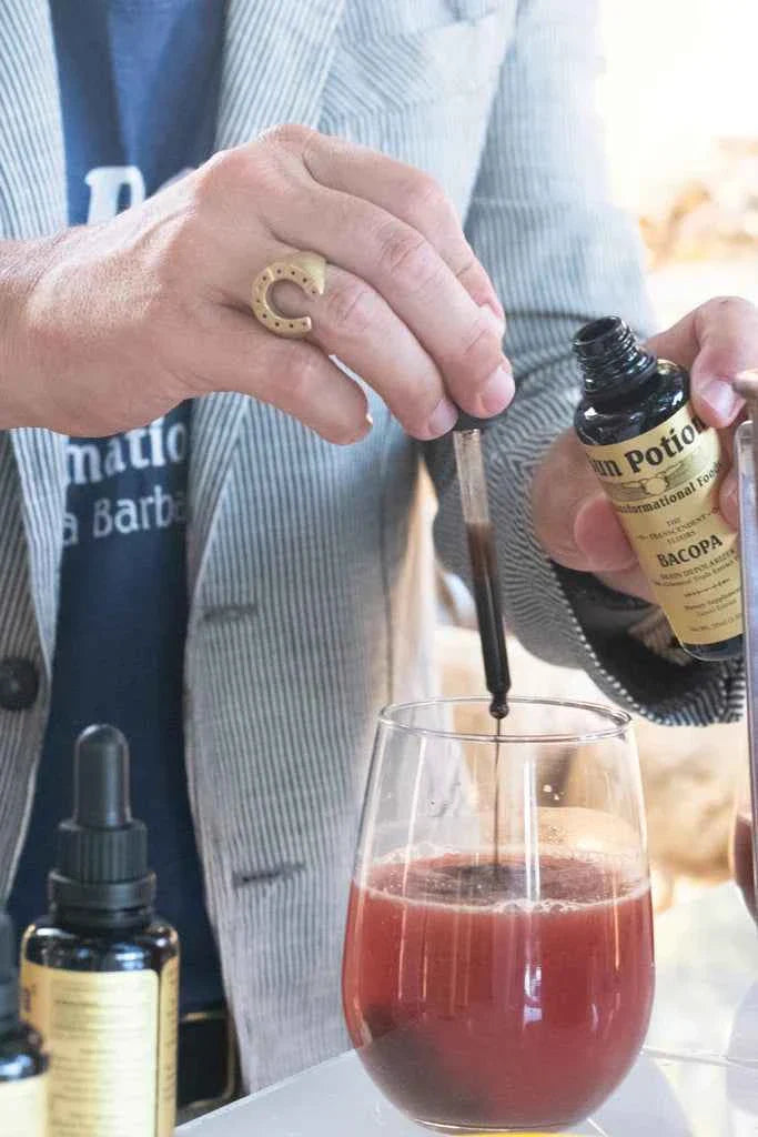 Hands dropping Sun Potion Bacopa Transcendent Elixir into a glass of red juice