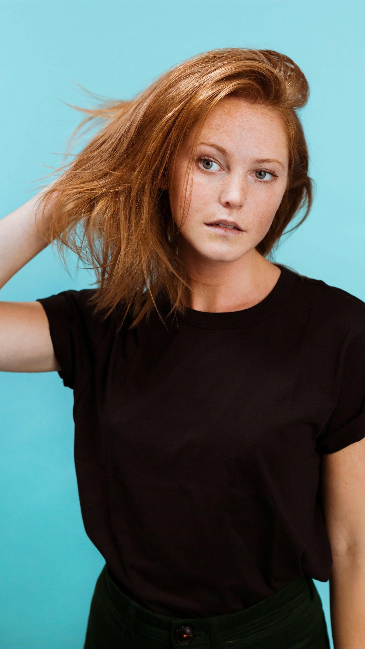 Woman with tousled red hair against a blue backdrop, styled with Firsthand Supply Texturizing Paste