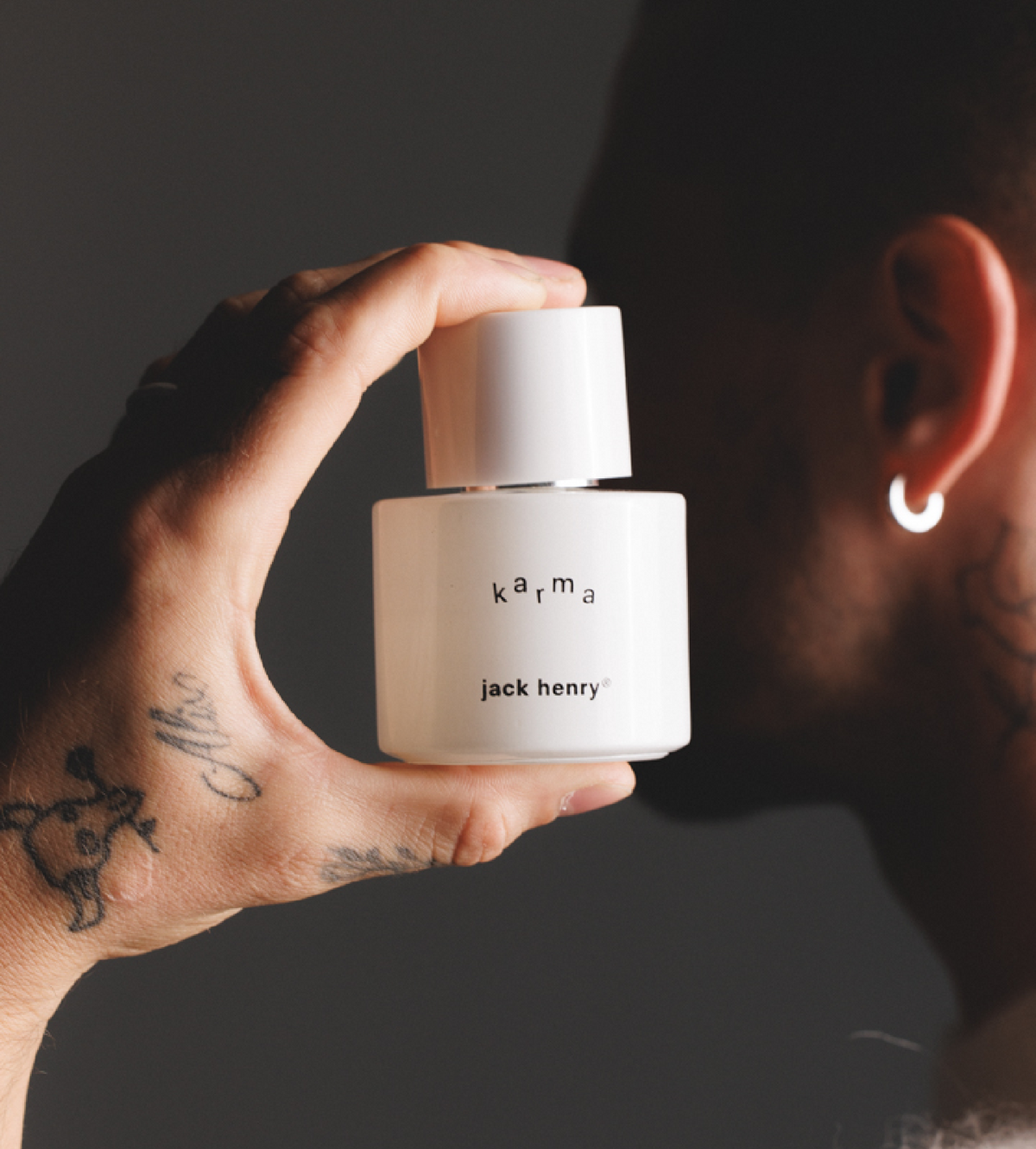 Man with a tattooed hand and earring holding a bottle of Jack Henry Karma