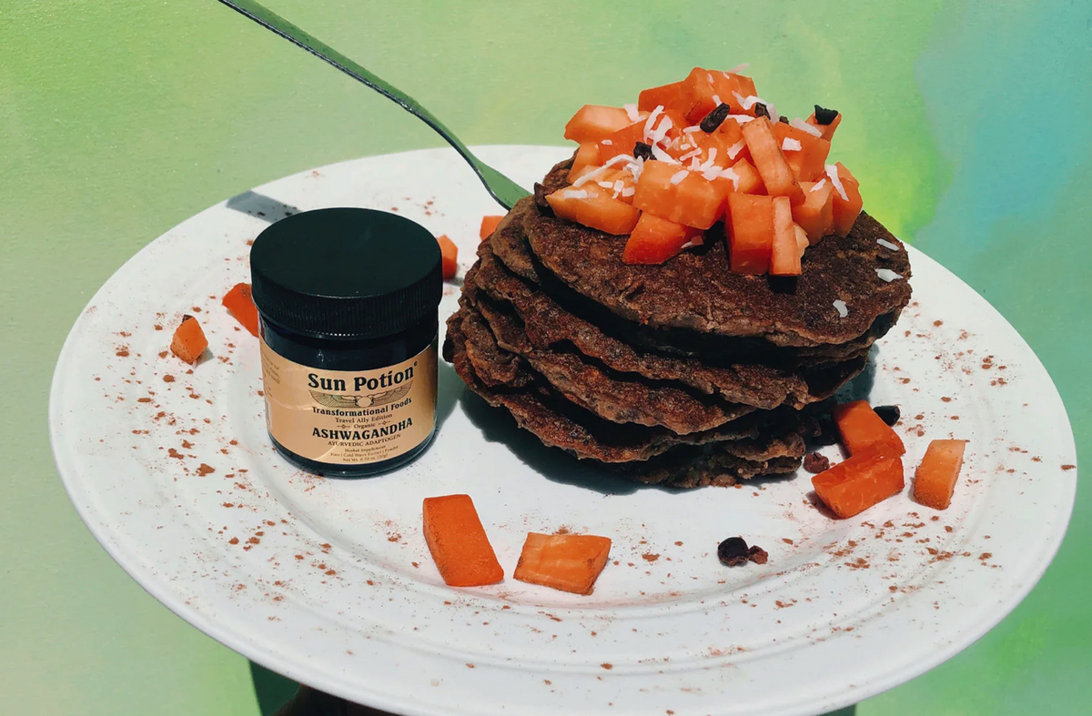 Sun Potion Ashwagandha jar beside a stack of chocolate pancakes topped with papaya