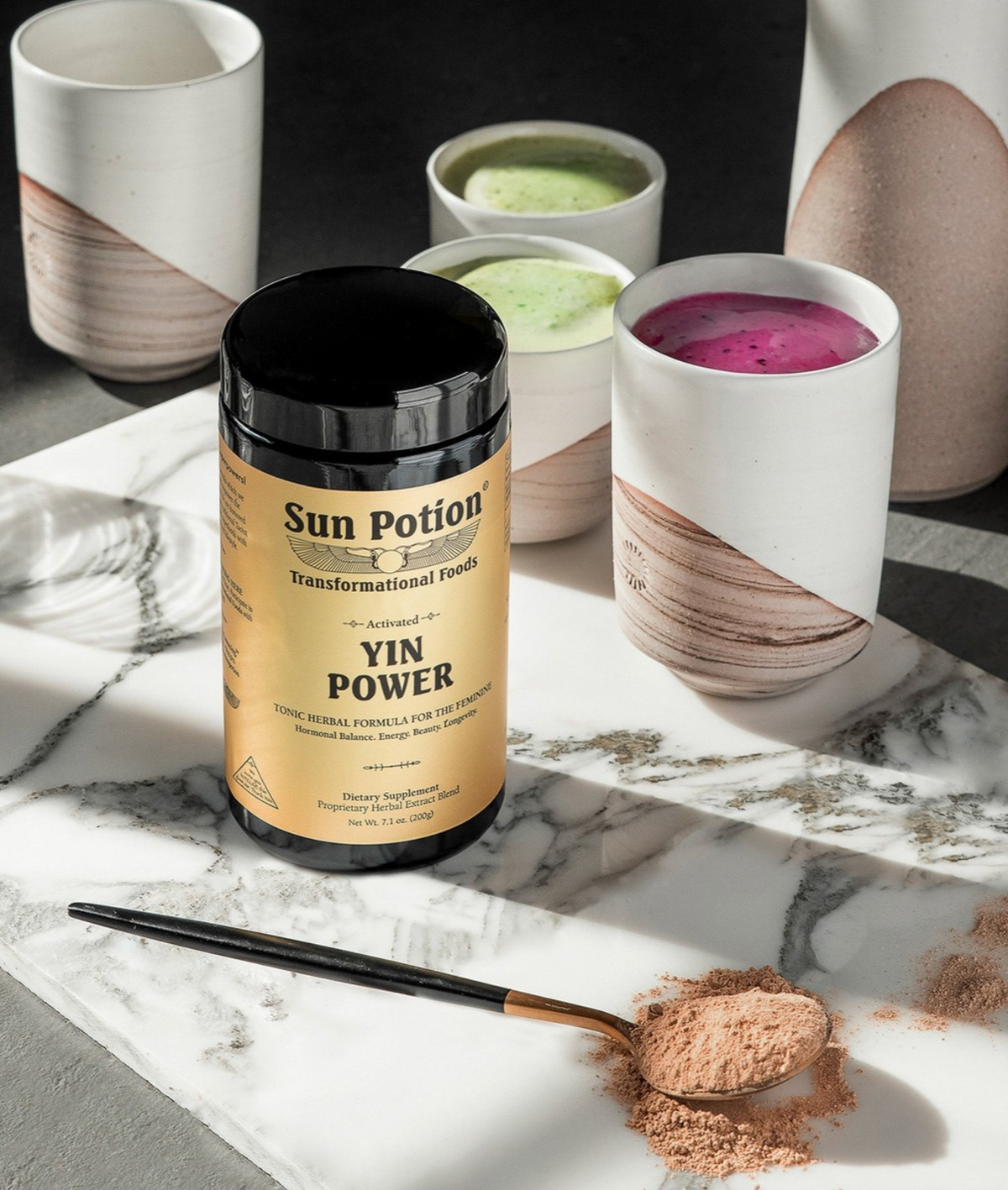 Sun Potion Yin Power jar on a marble table beside matcha and pink latte cups and a spoon of powder