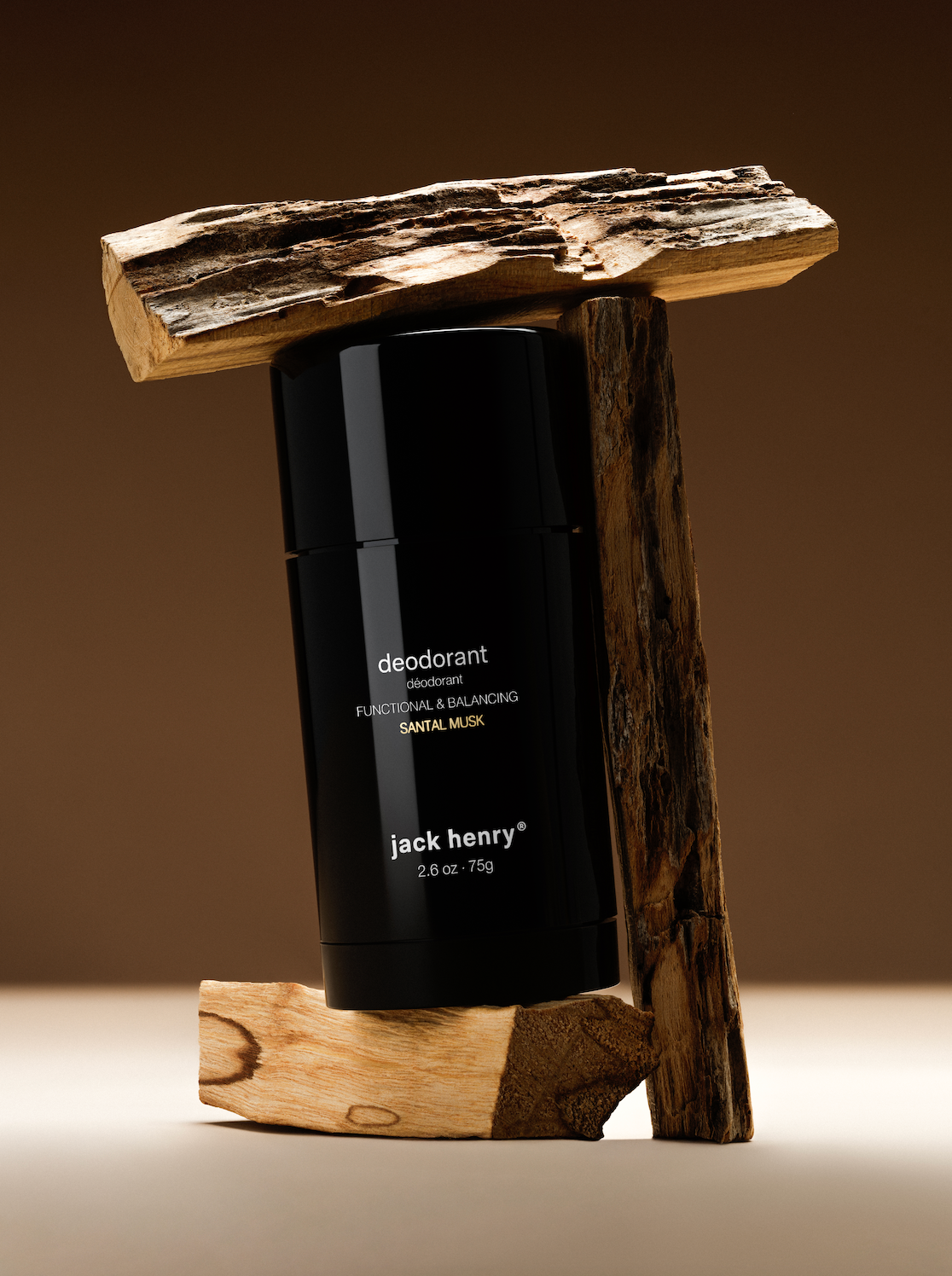 Jack Henry Deodorant in Sandal Musk balanced on a block of sandalwood