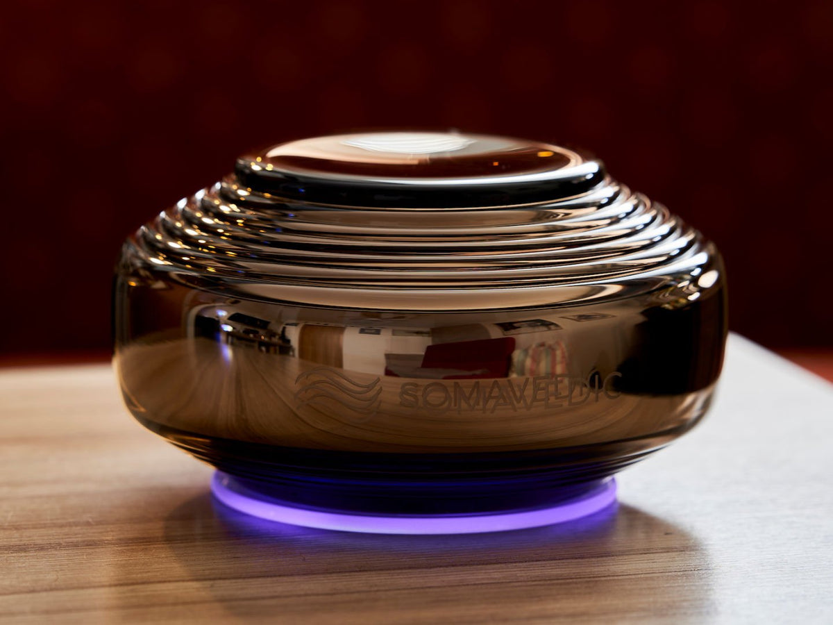 Close-up of the Somavedic Anthracite with a purple base glow on a wooden table