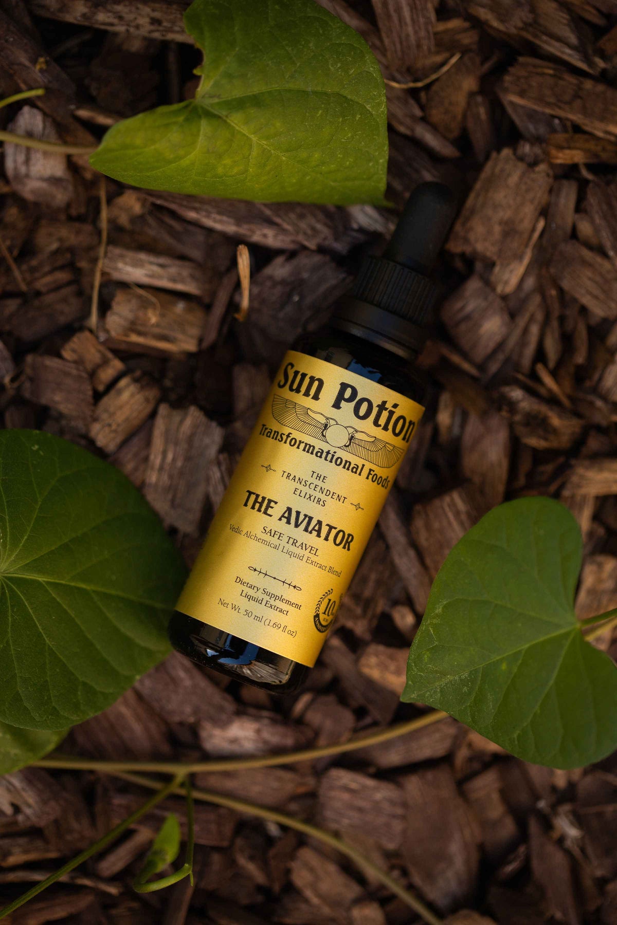 Sun Potion The Aviator Transcendent Elixir bottle lying on wood chips among green leaves