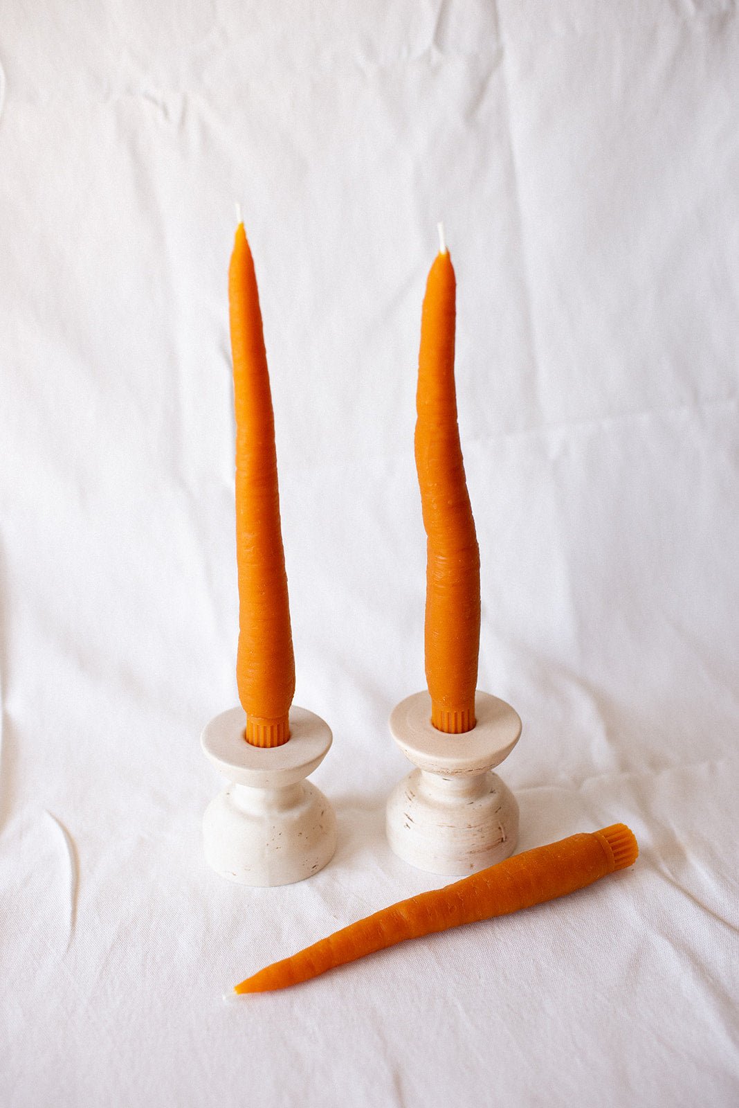 Happy Organics Carrot Beeswax Taper Candles in white holders beside a loose carrot candle