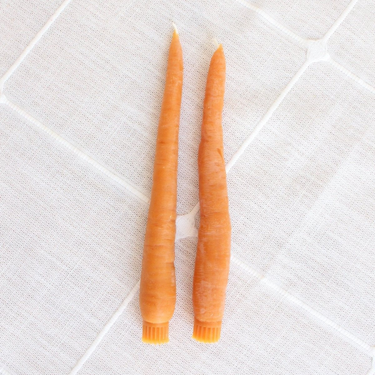 Happy Organics Carrot Beeswax Taper Candles lying on a white cloth