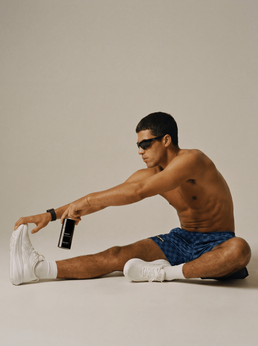 Man in blue shorts stretching on the floor holding a Jack Henry Deodorant
