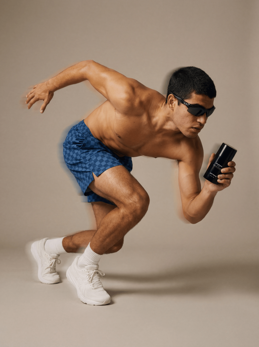 Man sprinting in blue shorts and sunglasses holding a Jack Henry Deodorant