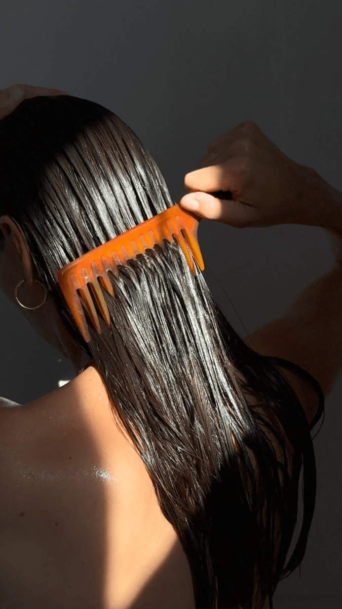 Firsthand Supply Everyday Conditioner: woman combing conditioner through long wet hair with an orange wide-tooth comb
