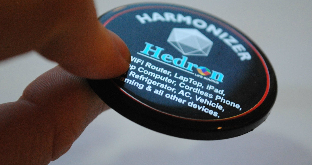 Finger holding the Hedron Life Source Harmonizer disc with its device list printed on the face