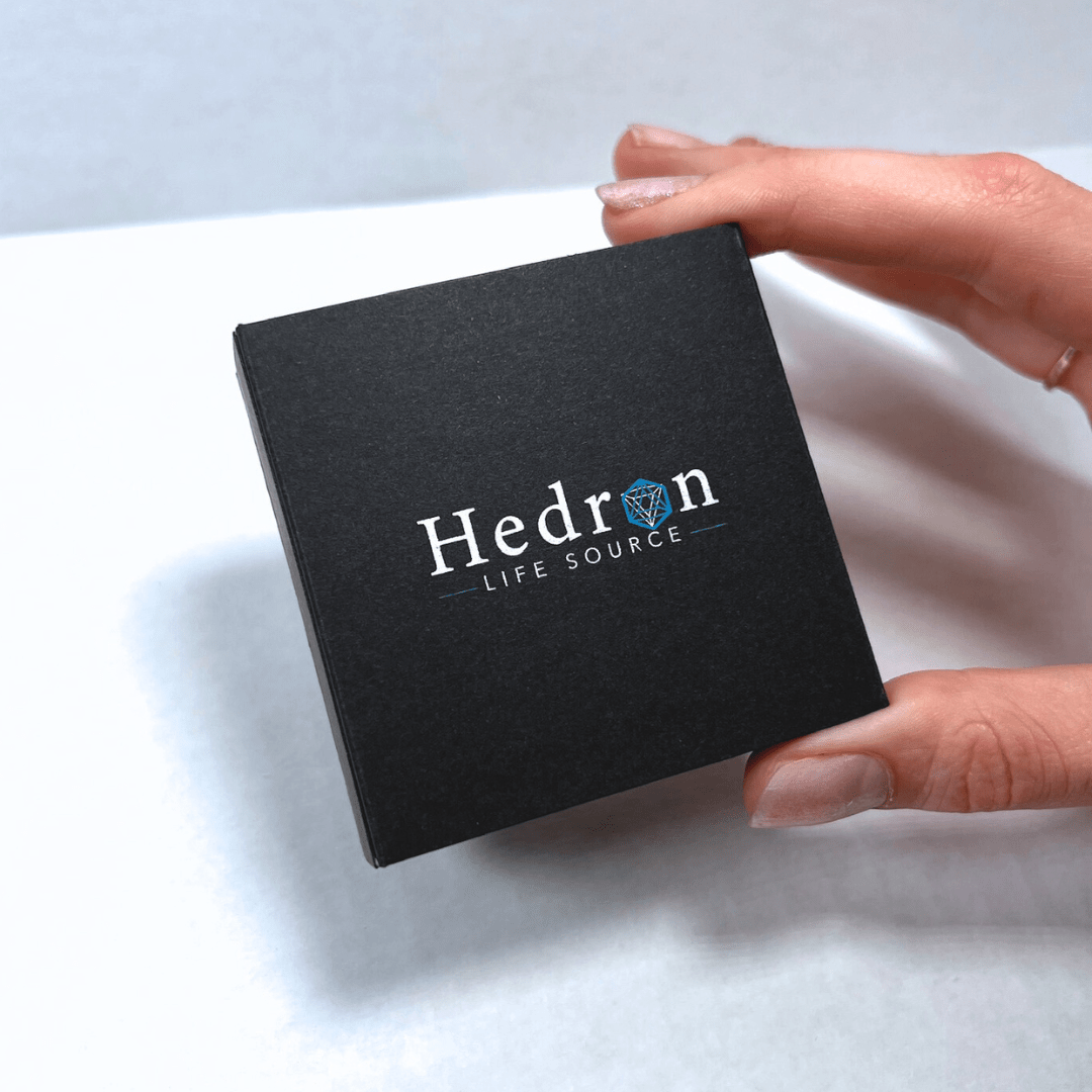 Hand holding the black Hedron Life Source Harmonizer gift box with the Hedron logo