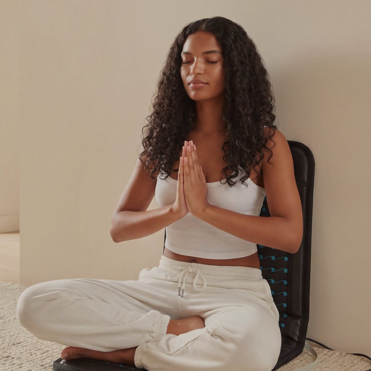 Woman meditating with her hands together against the HigherDOSE Infrared PEMF Go Mat on her back