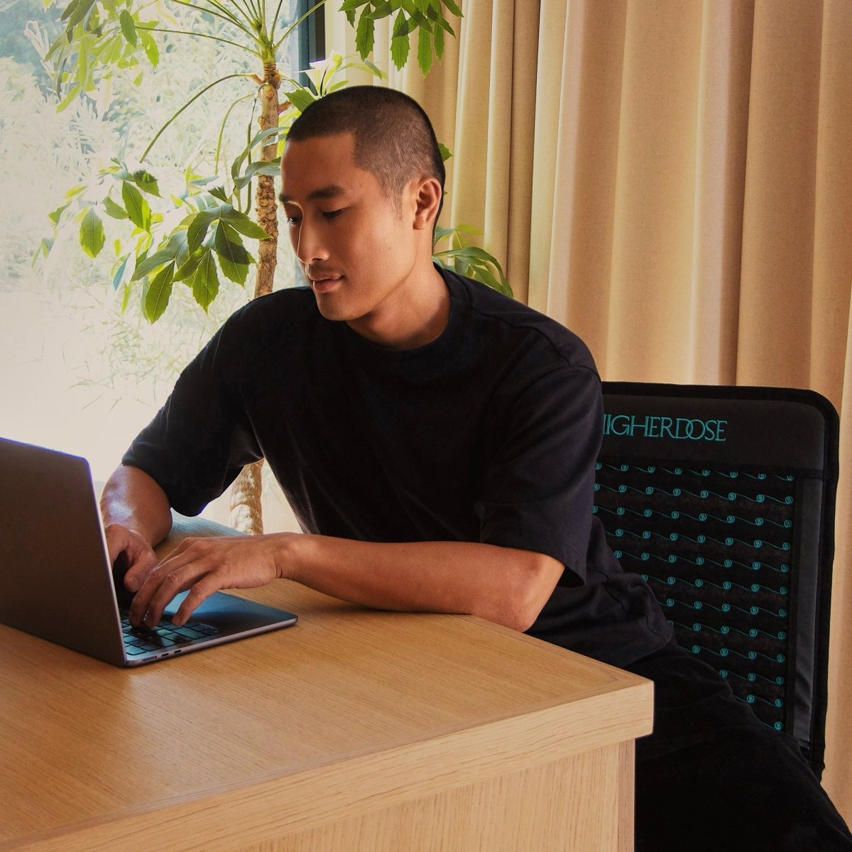 Man working on a laptop at a desk with the HigherDOSE Infrared PEMF Go Mat on his chair