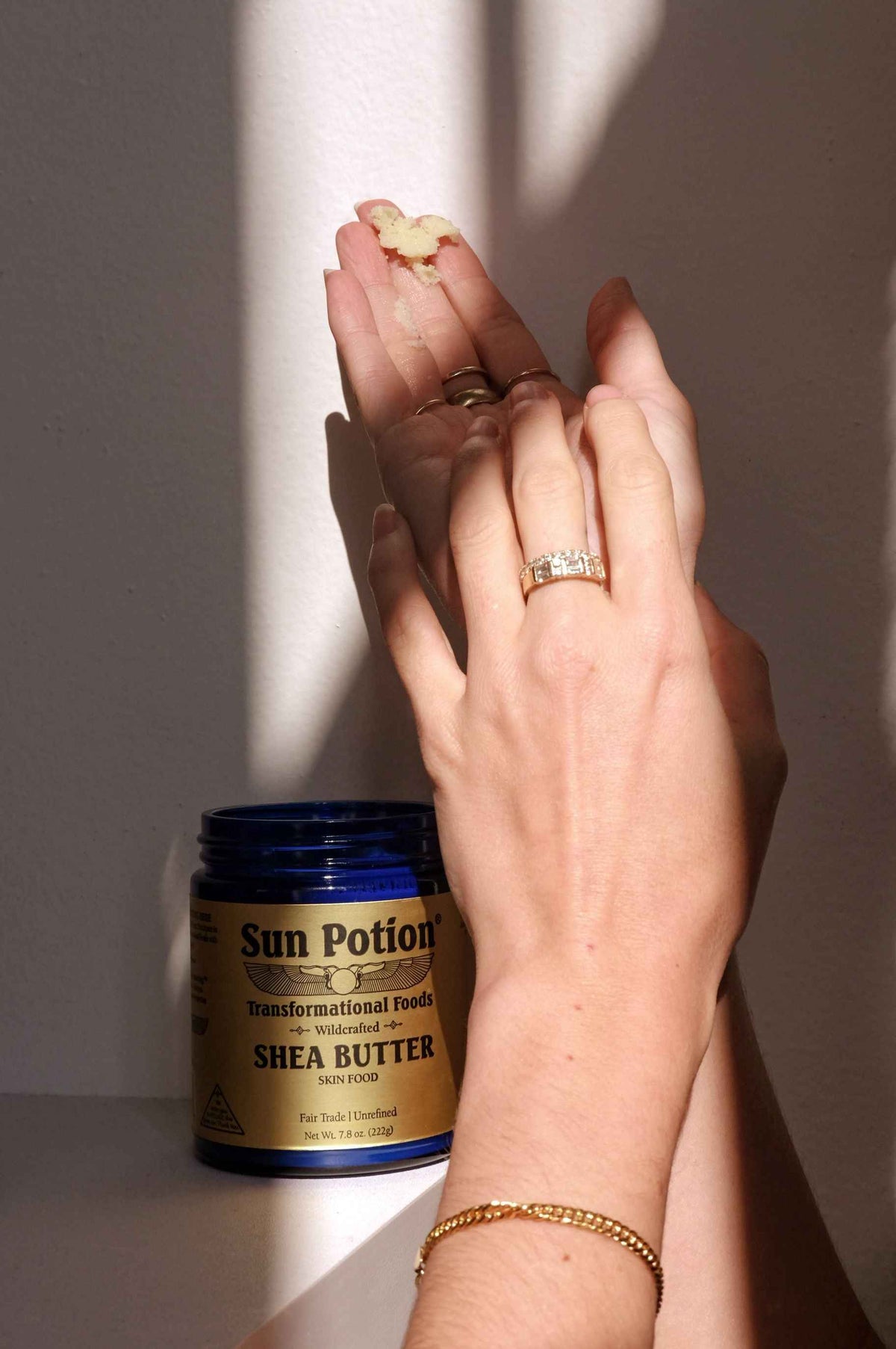 Hands applying Sun Potion Shea Butter to the skin with a jar of shea butter in the foreground