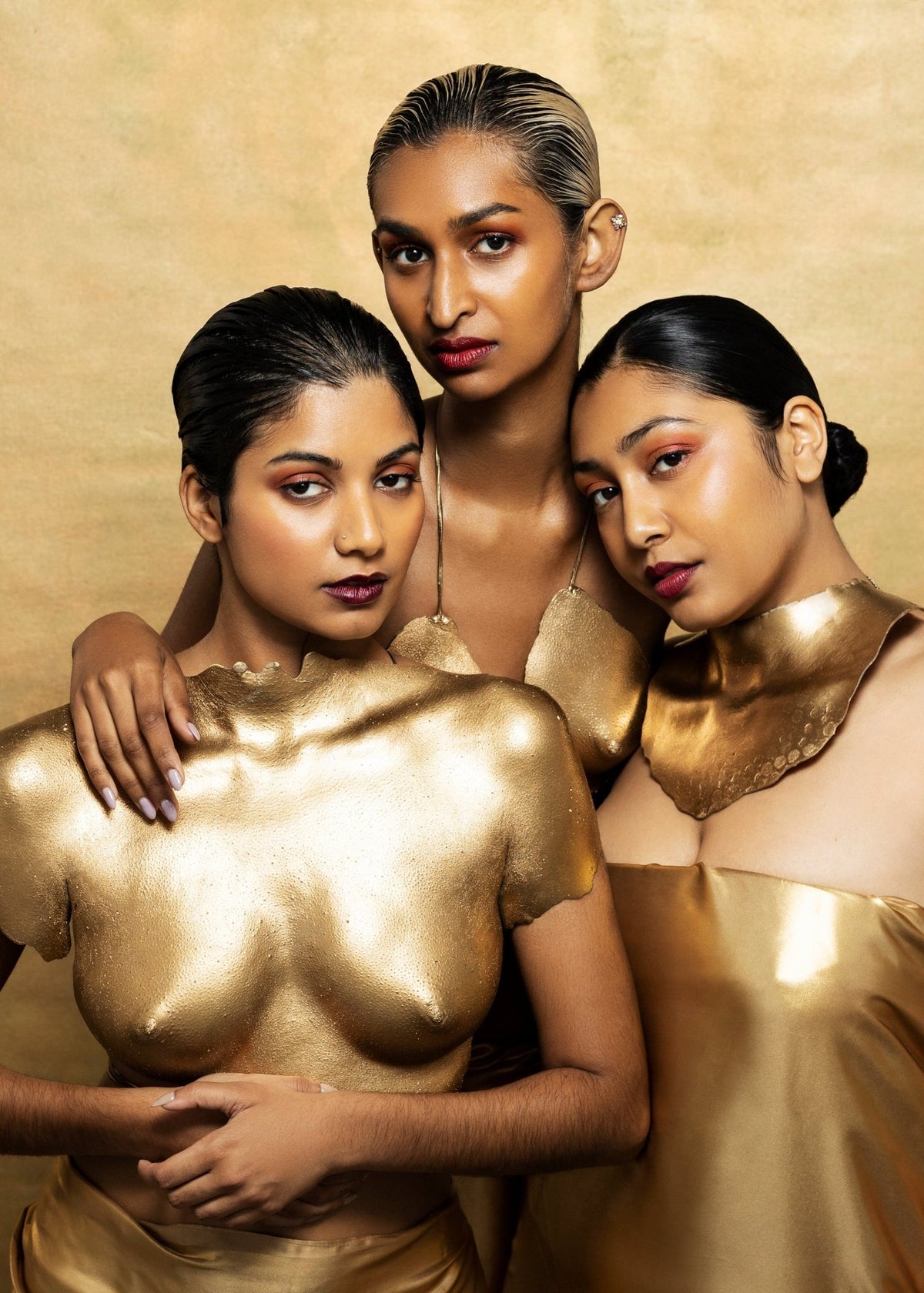Three women with gold body paint against a gold backdrop, the TANAÏS Lovers Rock Extrait de Parfum campaign