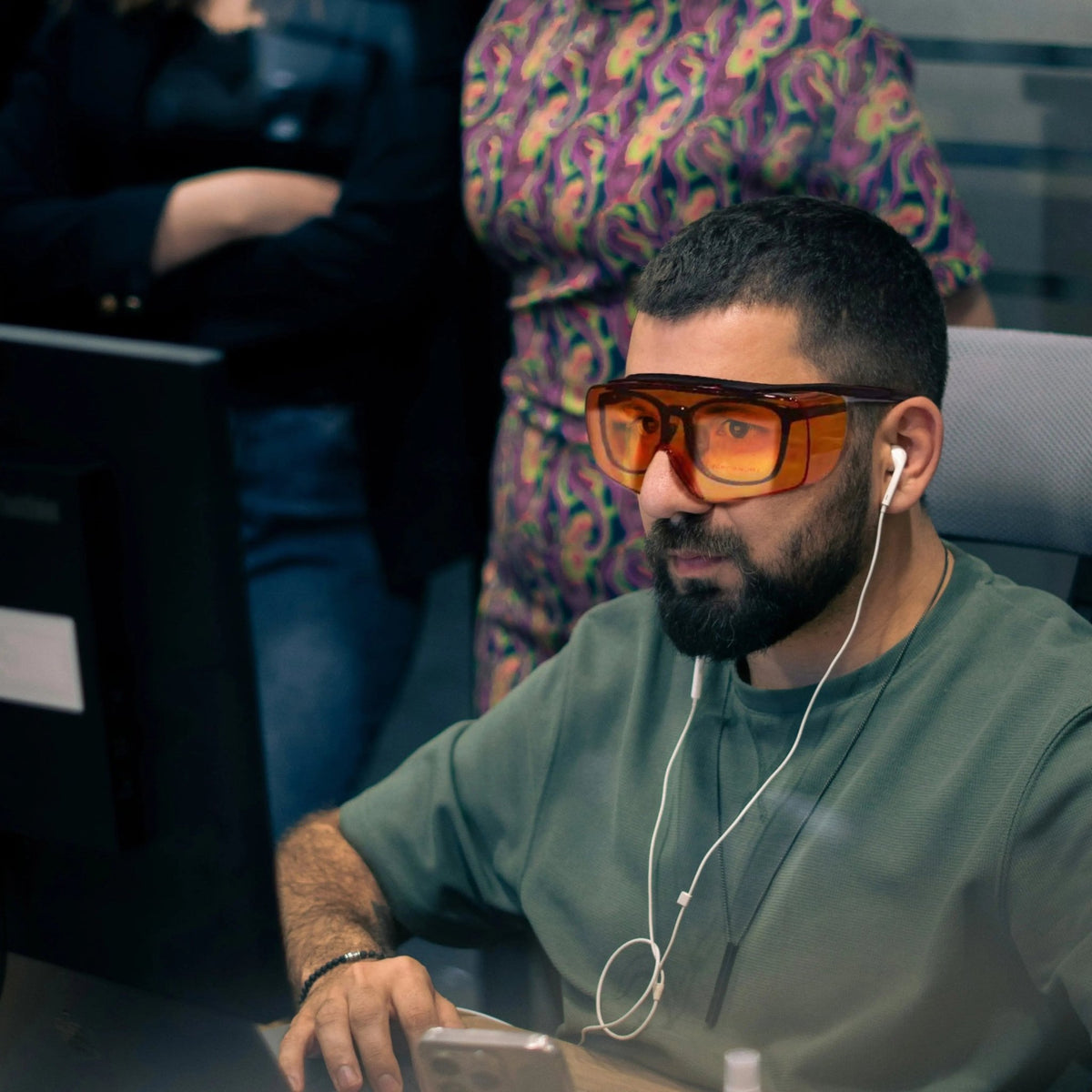 Man with a beard at a desk wearing Lumos Sleep Blue Blocker orange glasses and earbuds