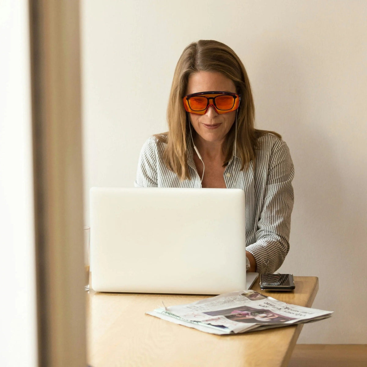 Woman at a laptop with a newspaper wearing Lumos Sleep Blue Blocker orange glasses