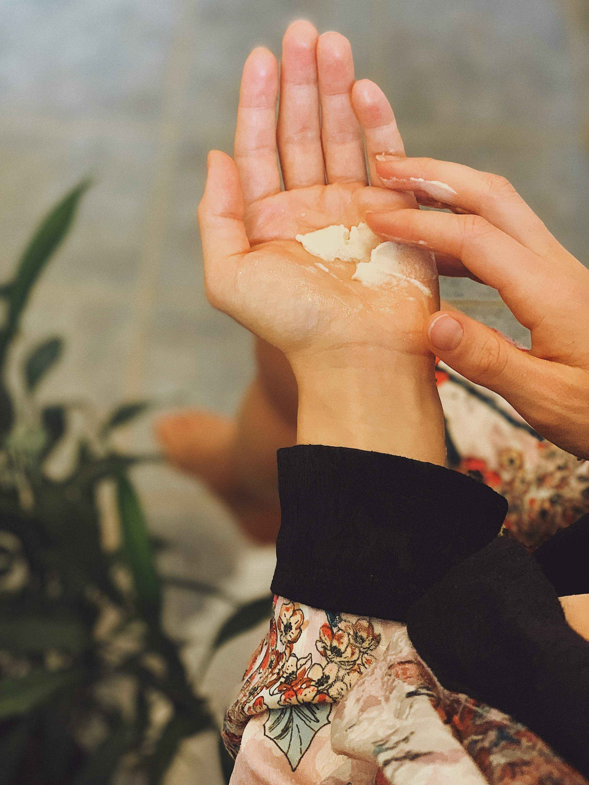 Hands rubbing Sun Potion Shea Butter on a wrist among green leaves