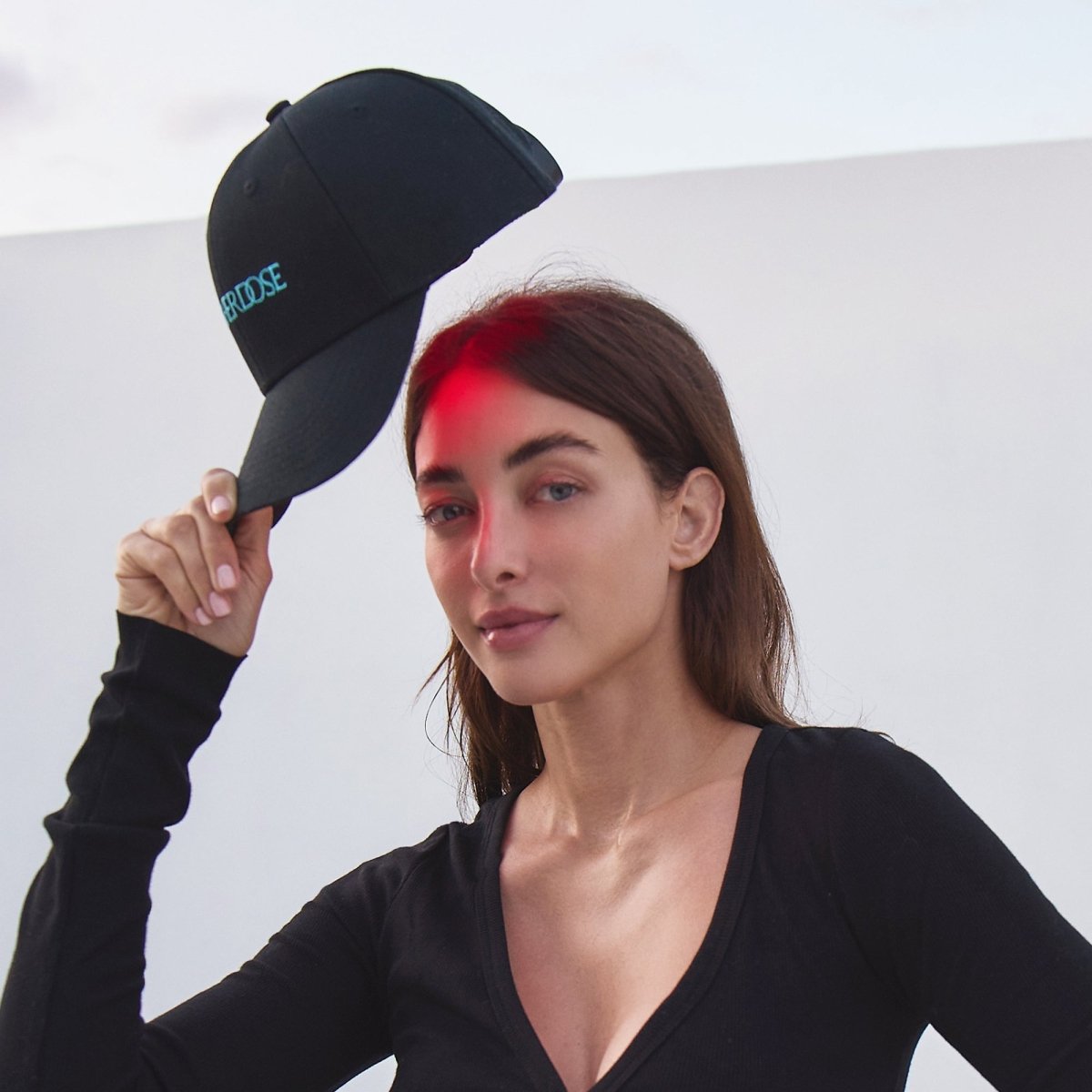 Woman in a black top wearing the HigherDOSE Red Light Hat with a red glow on her forehead