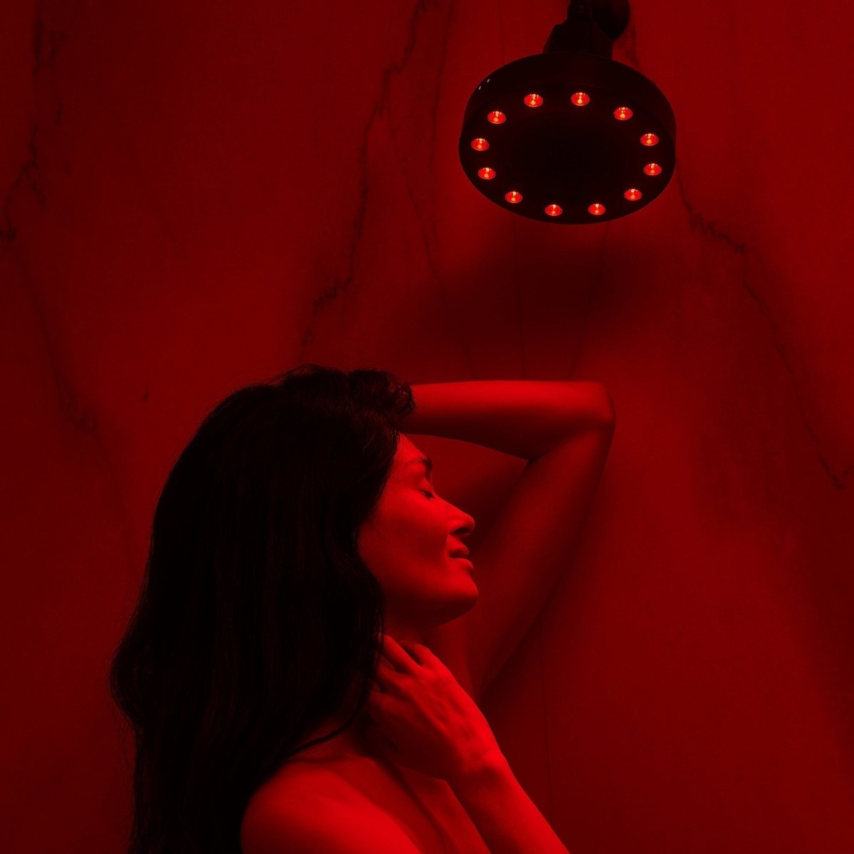 Woman in a red-lit shower under the black HigherDOSE Red Light Showerhead Filter