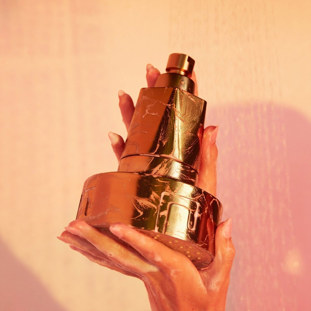Hands holding a gold HigherDOSE showerhead filter cartridge against a peach background