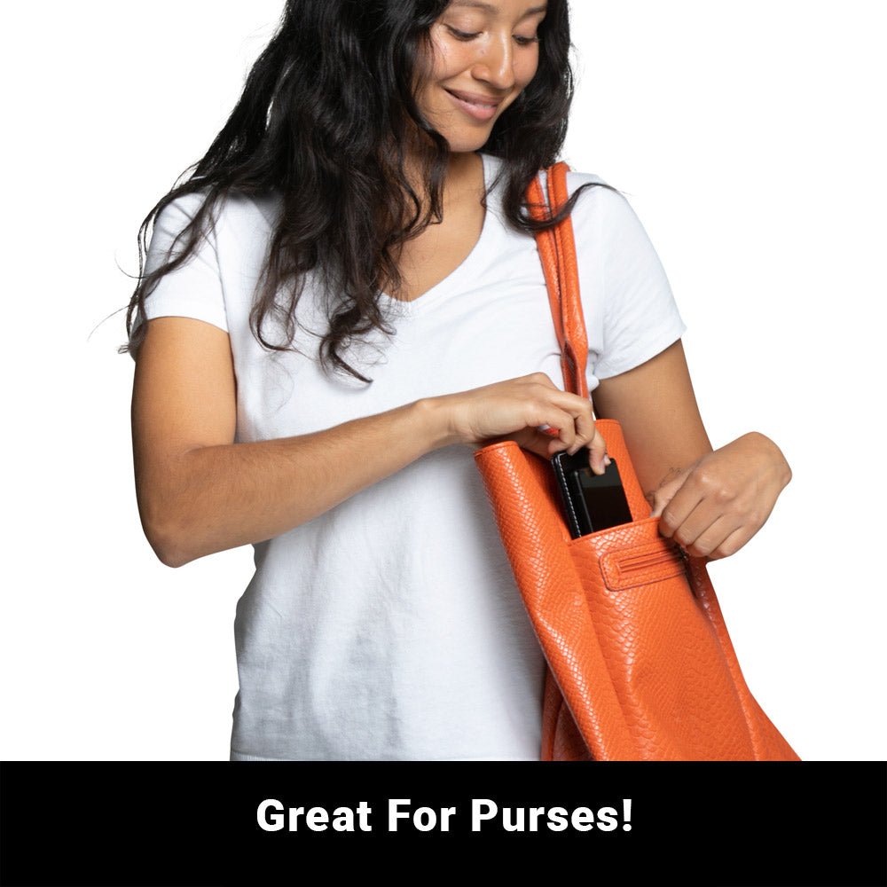 Woman putting a phone and the Shield Your Body Phone Shield into an orange purse