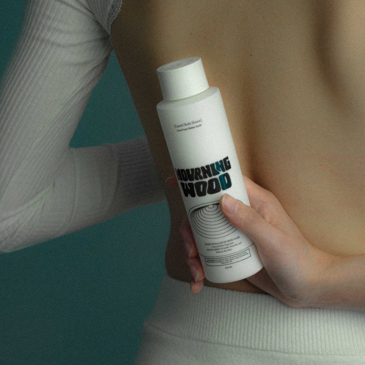 Hands holding the Laurel Bath House Mourning Wood body wash bottle against a woman's back