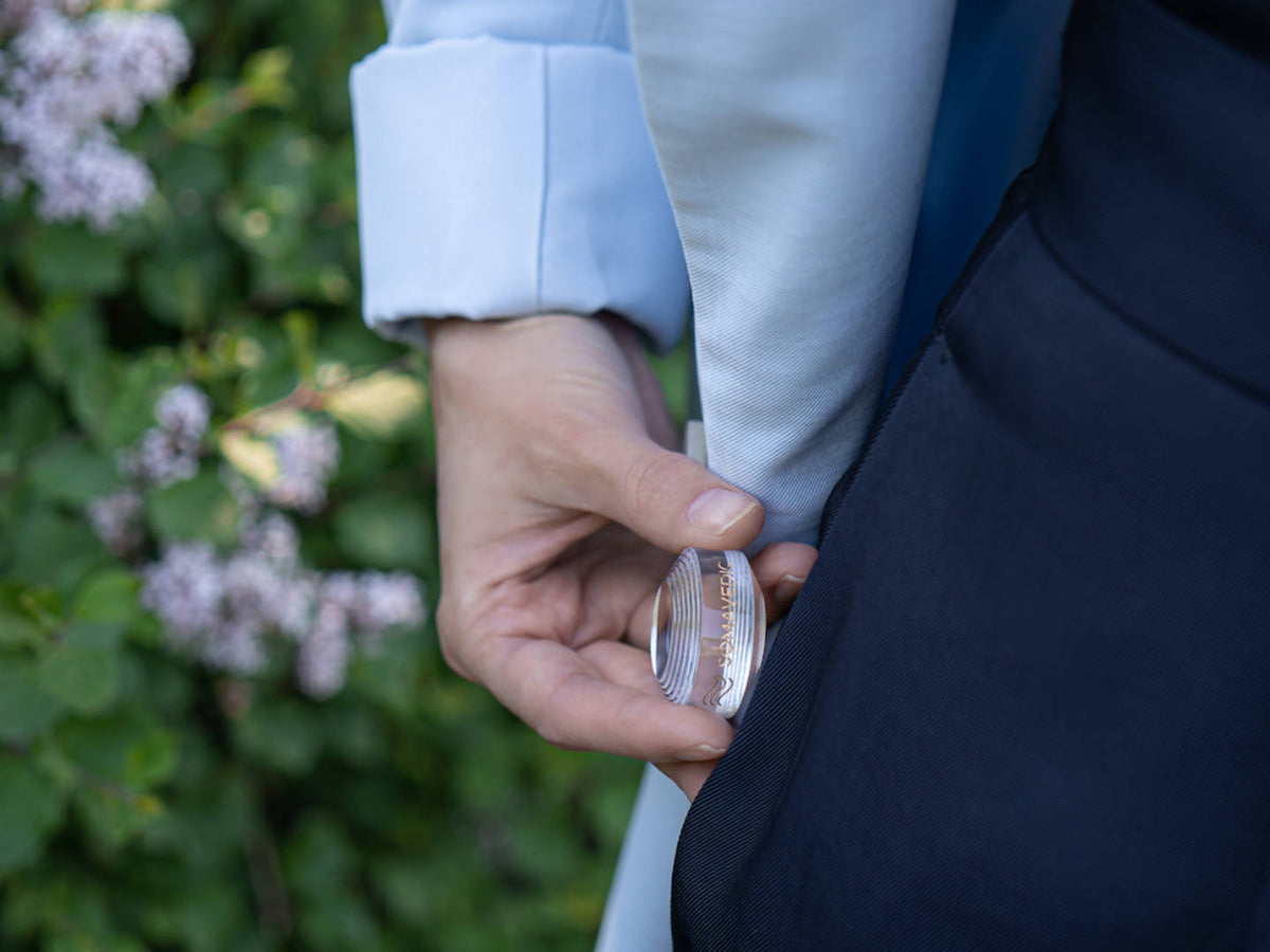 Hand placing the Somavedic Tiny clear into a jacket pocket among lilac flowers