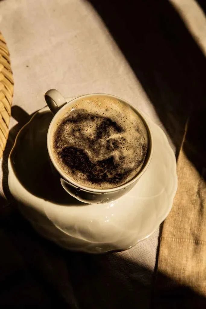 Cup of dark latte on a saucer in dappled light, made with Sun Potion Yin Power