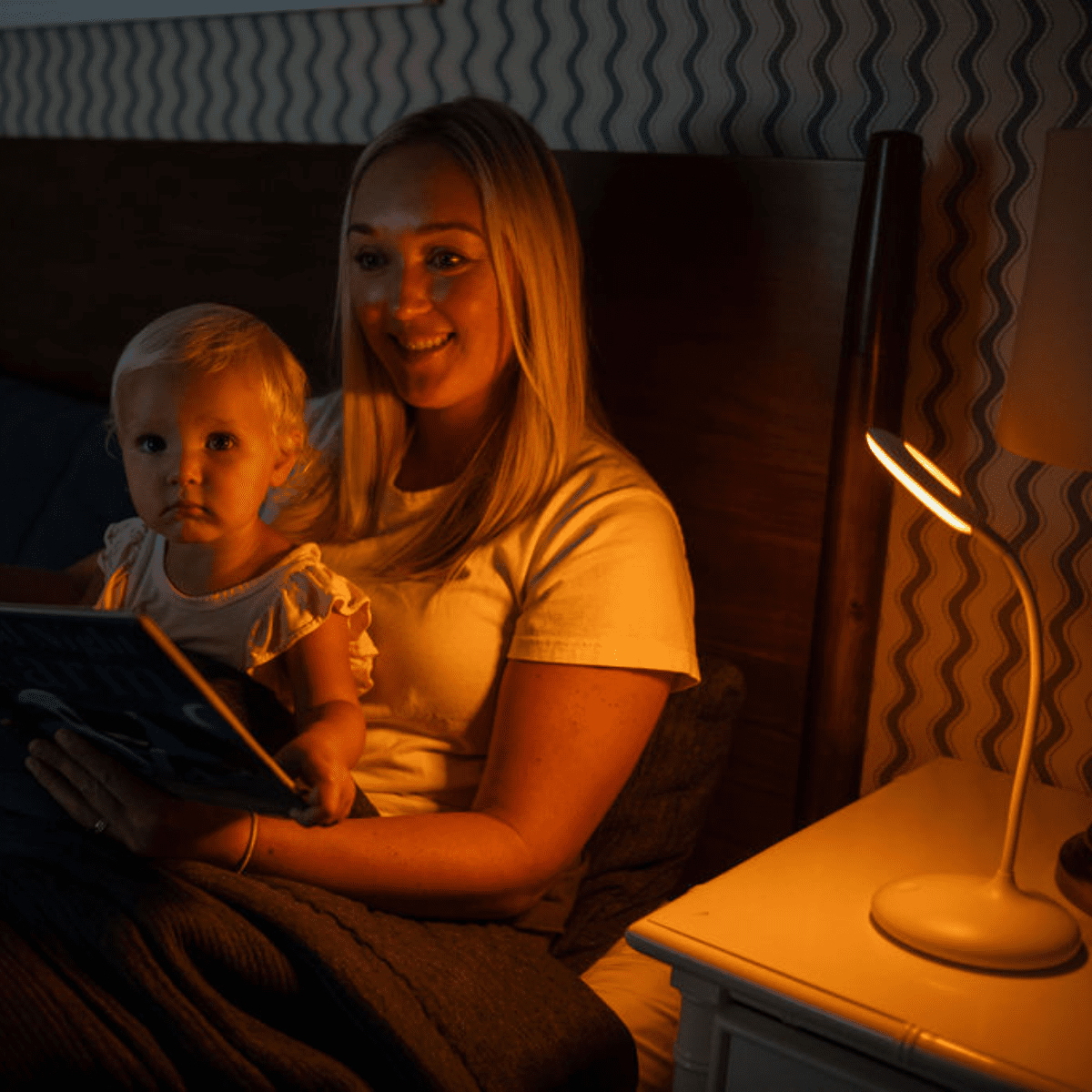 Blond mother reading to a young blond child on her lap using a circadian lamp on nanaka.co