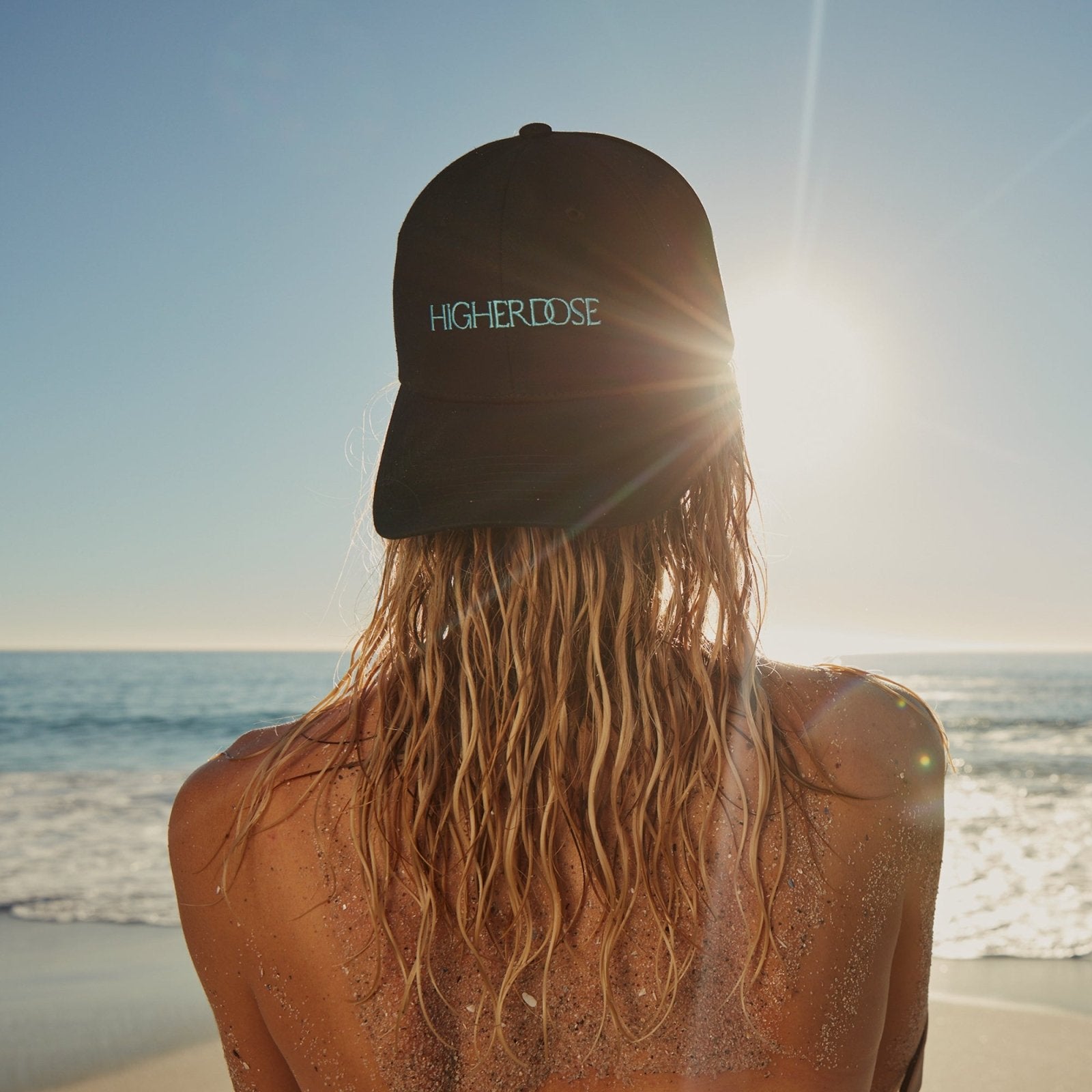 Woman wearing the HigherDOSE Red Light Hat backwards on a beach