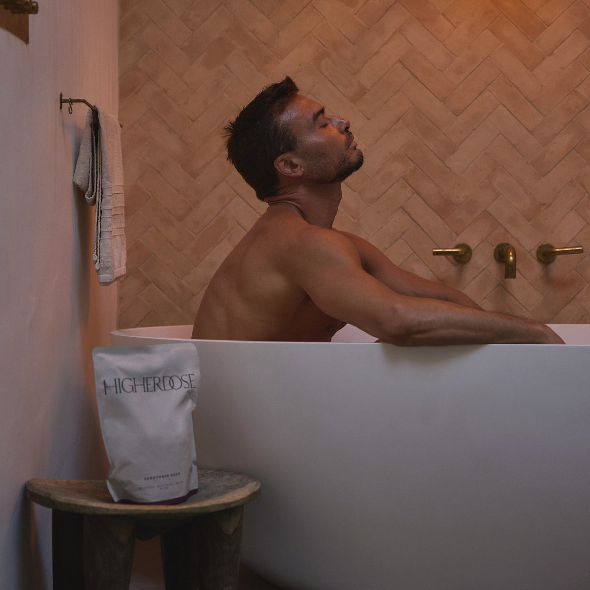 Man relaxing in a bathtub beside the HigherDOSE Serotonin Soak bag