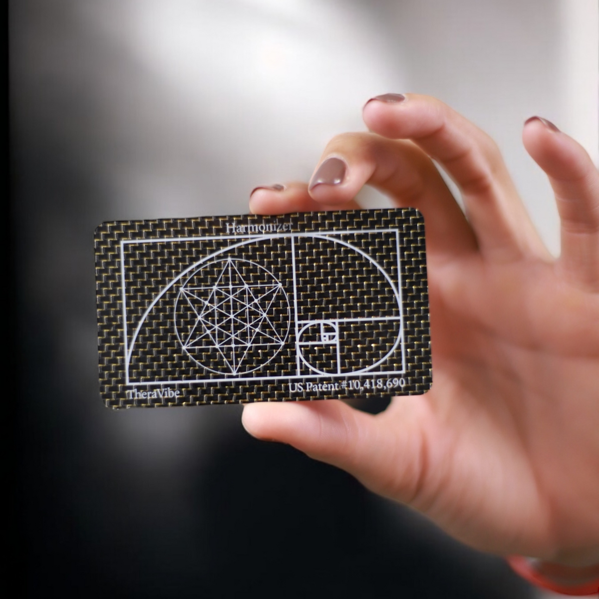 Hand holding a Therasage TheraVibe Quantum Card showing the golden ratio spiral design