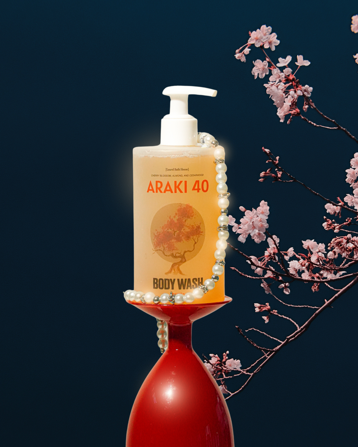Laurel Bath House Araki 40 body wash bottle on a red glass stand draped in pearls beside cherry blossoms