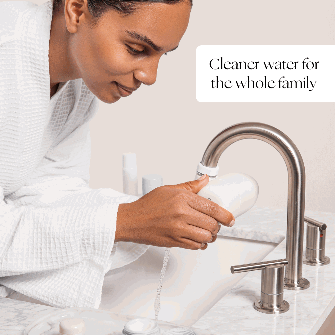 Woman in a white robe using a Canopy Faucet Filter at a bathroom sink: cleaner water for the whole family