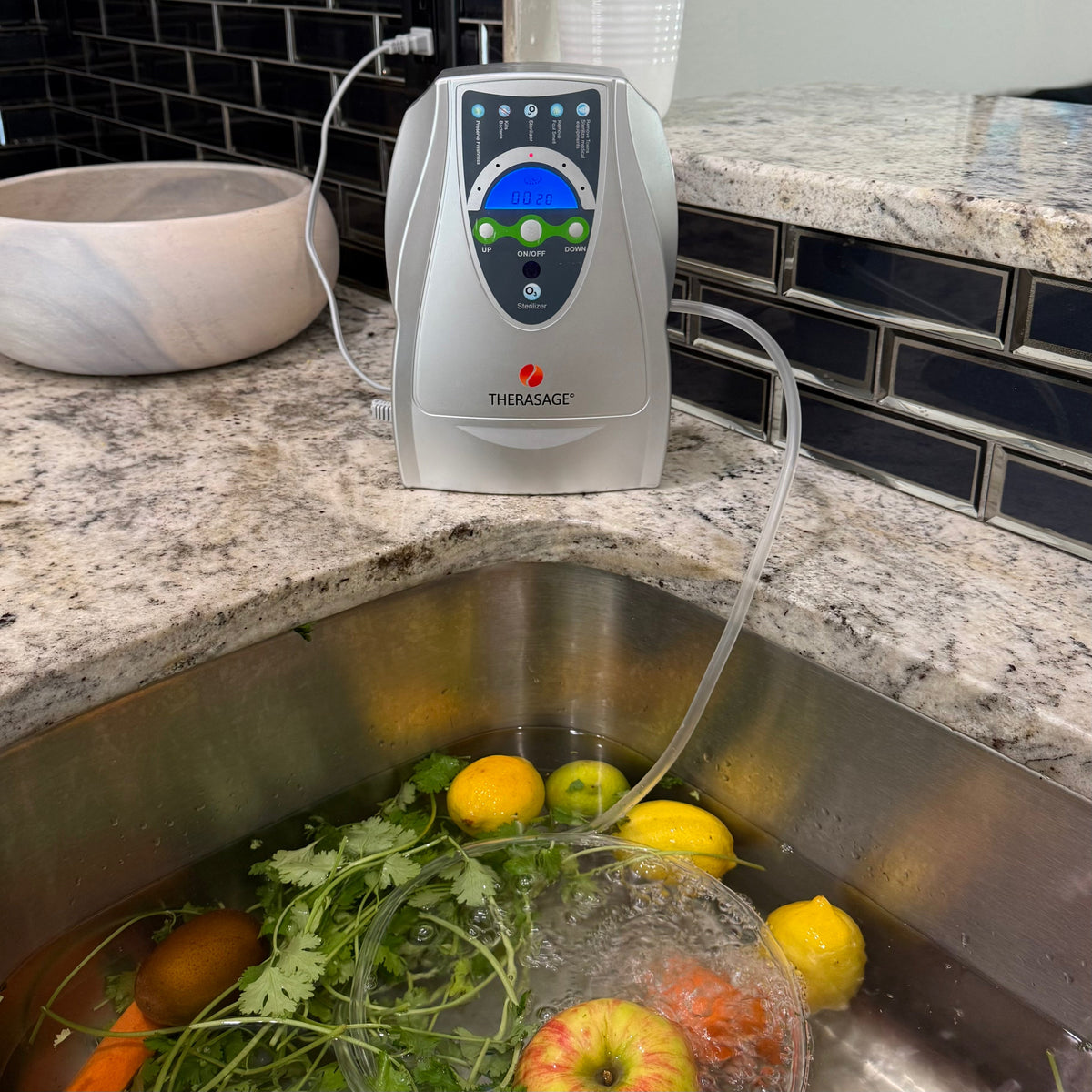 Therasage TheraO3 Ozone Bubbler on a kitchen counter with tubing running into a sink of fruit and greens