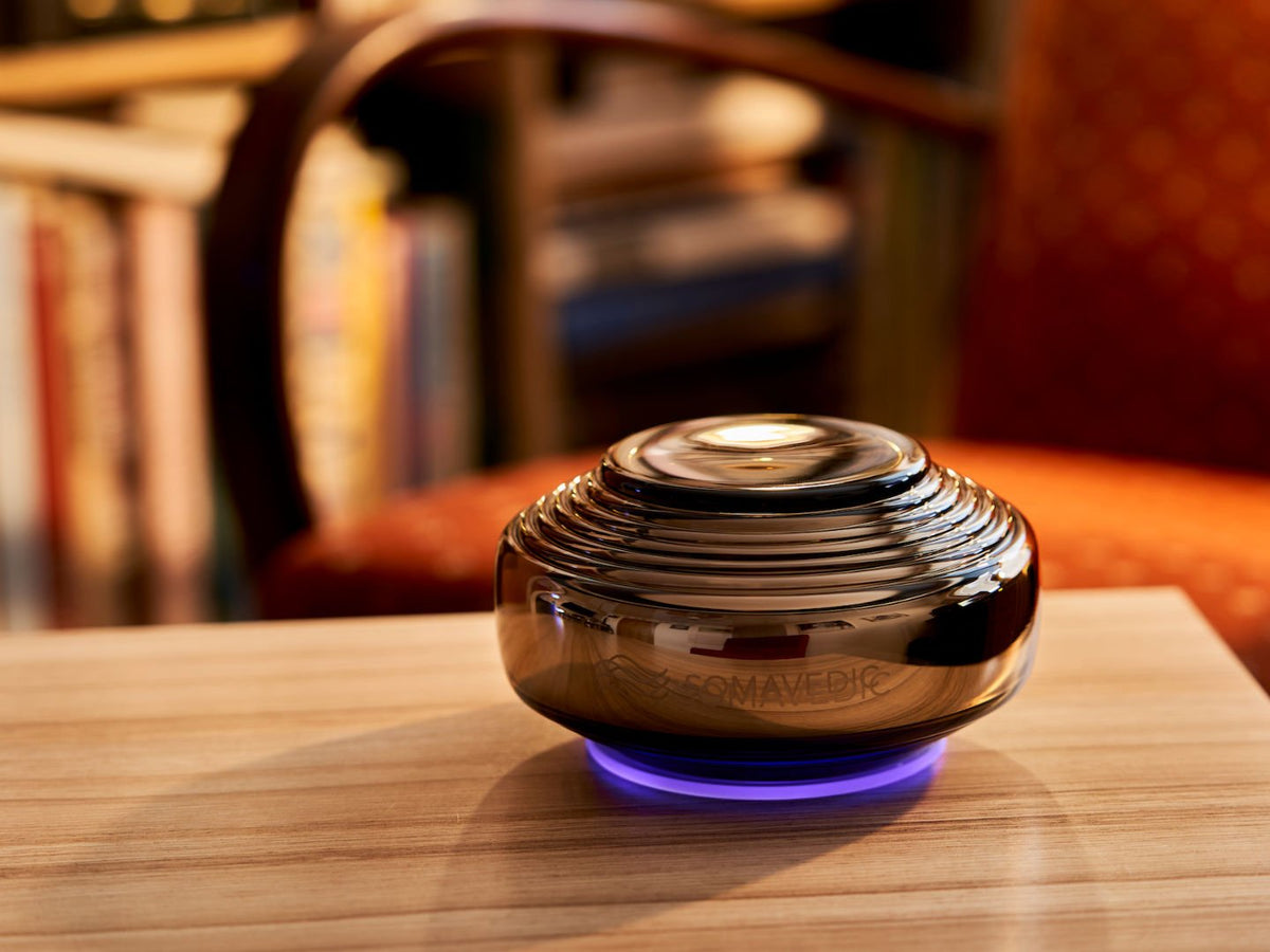 Somavedic Anthracite glowing on a wooden table in a living room with bookshelves