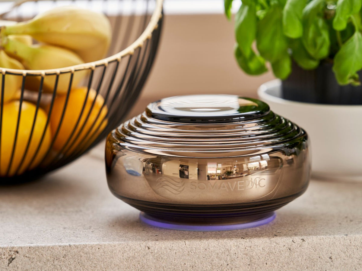 Somavedic Anthracite on a stone counter beside a fruit bowl and basil plant
