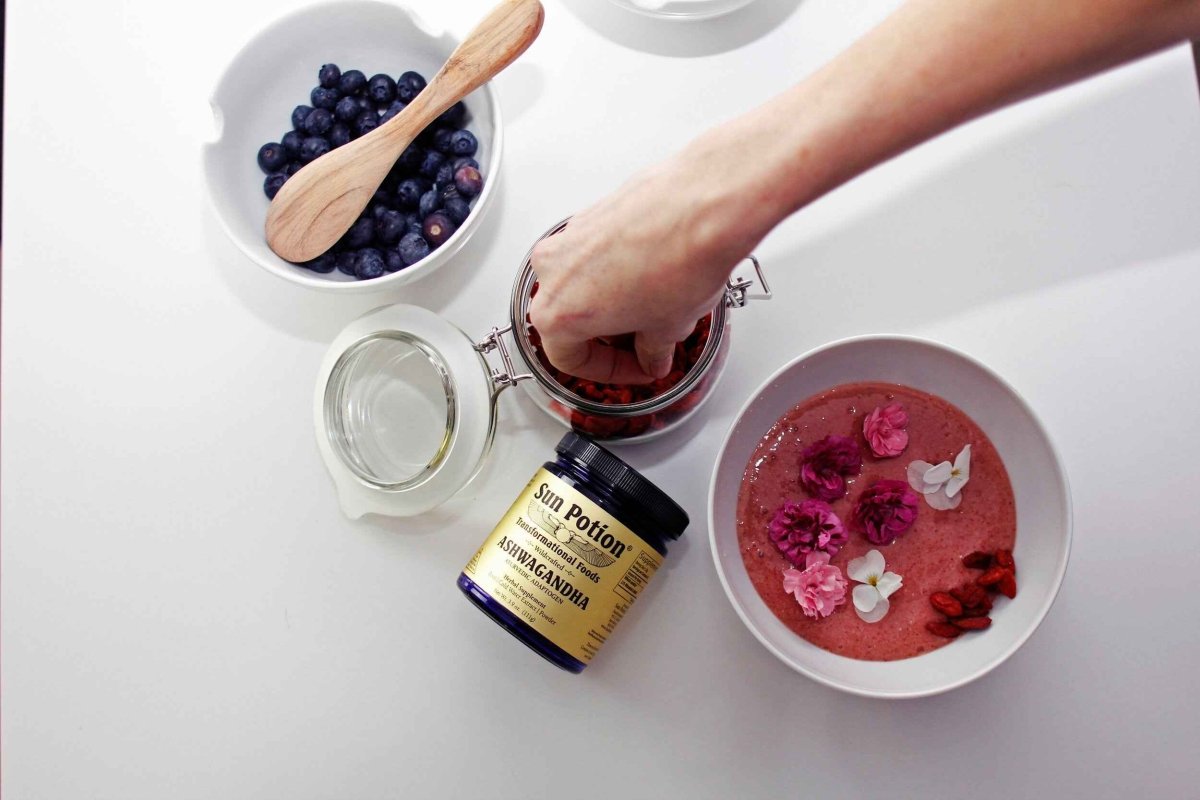 Hand reaching for a Sun Potion Ashwagandha jar beside a bowl of berries and a smoothie bowl