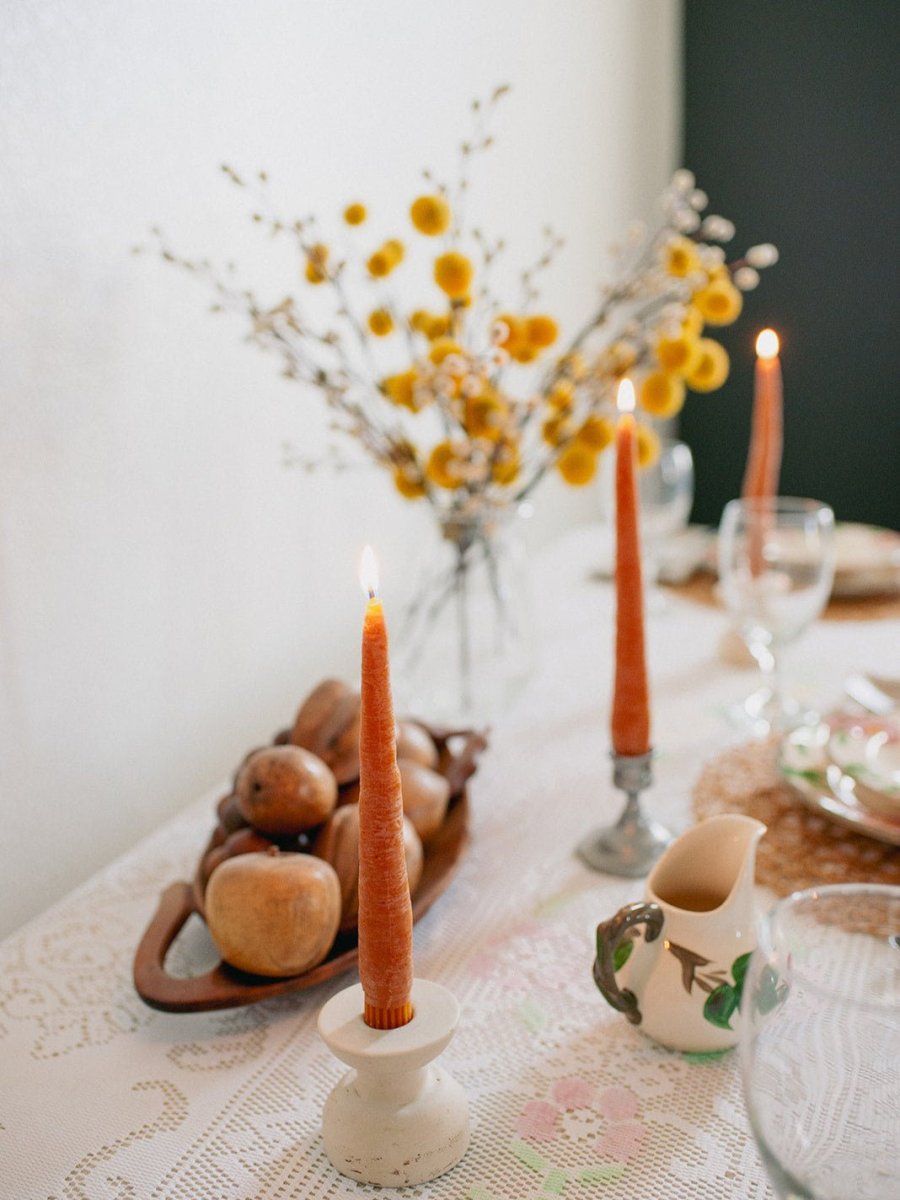 Lit Happy Organics Carrot Beeswax Taper Candles on a set dinner table with flowers