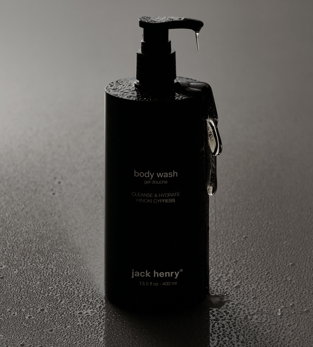 Jack Henry Body Wash pump bottle covered in water droplets on a dark background