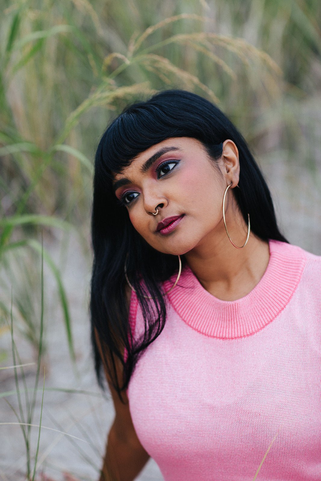 Woman with dark bangs and hoop earrings wearing TANAÏS Heart Chakra Mood Change Lip Stain by tall grass