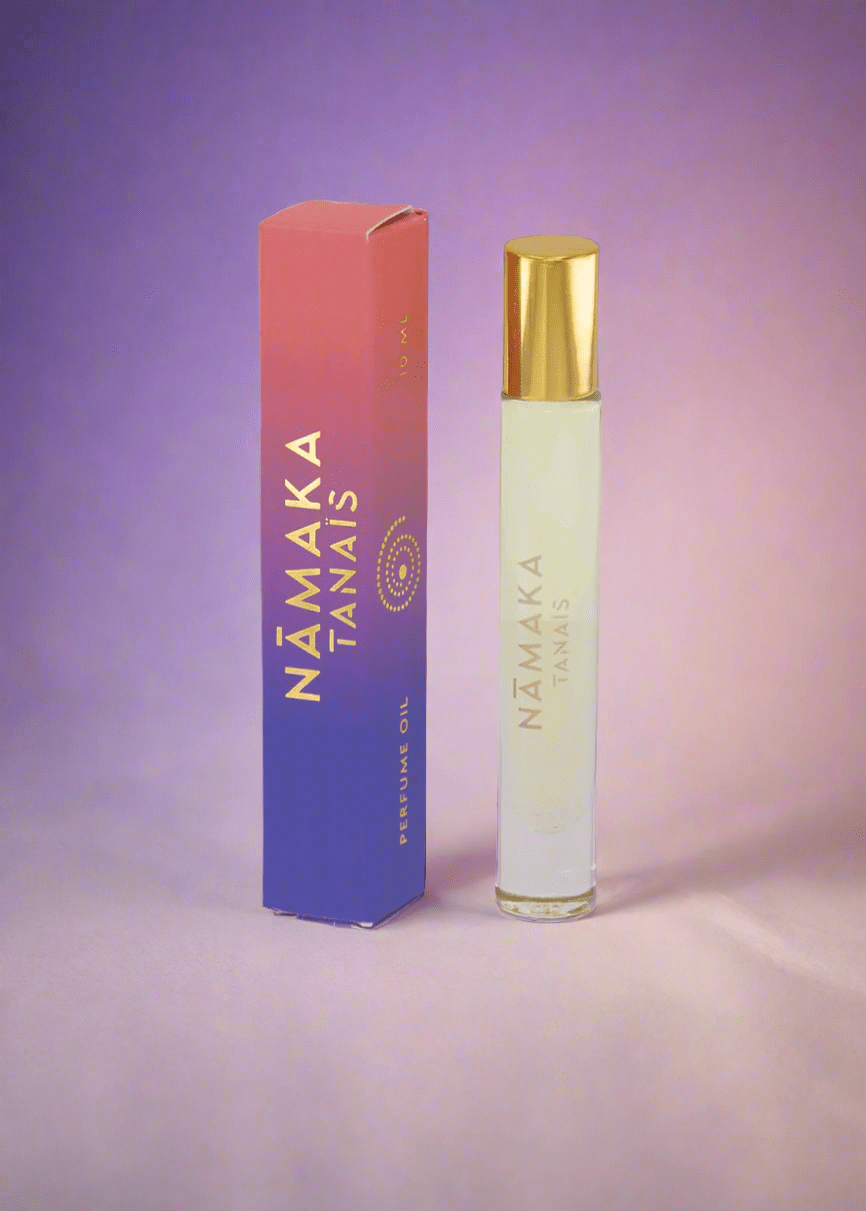 TANAÏS Nāmaka Perfume Oil roll-on bottle beside its blue and pink box on a purple background